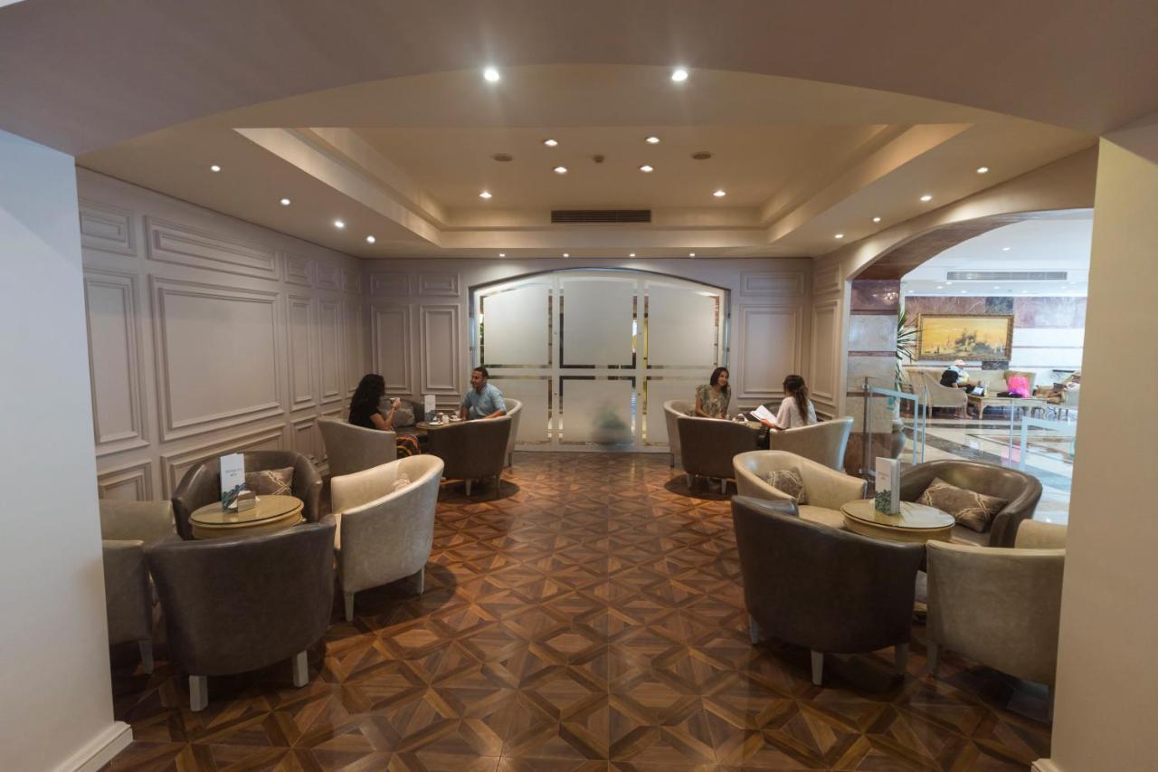 โรงแรมซันไรส์ อเล็กซ์ อเวนิว อเล็กซานเดรีย ภายนอก รูปภาพ The photo shows a well-lit lounge area with a modern and elegant design. There are several comfortable seating arrangements, including plush chairs and small tables. The flooring appears to be made of a decorative wood pattern. In the background, the