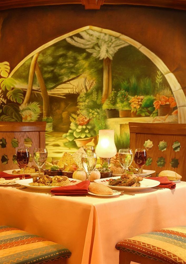 โรงแรมซันไรส์ อเล็กซ์ อเวนิว อเล็กซานเดรีย ภายนอก รูปภาพ The photo depicts a beautifully arranged dining table set against a vibrant mural of a garden. The table features a variety of dishes, likely a mix of main courses and sides, elegantly presented on white plates. There are also several glasses, includ