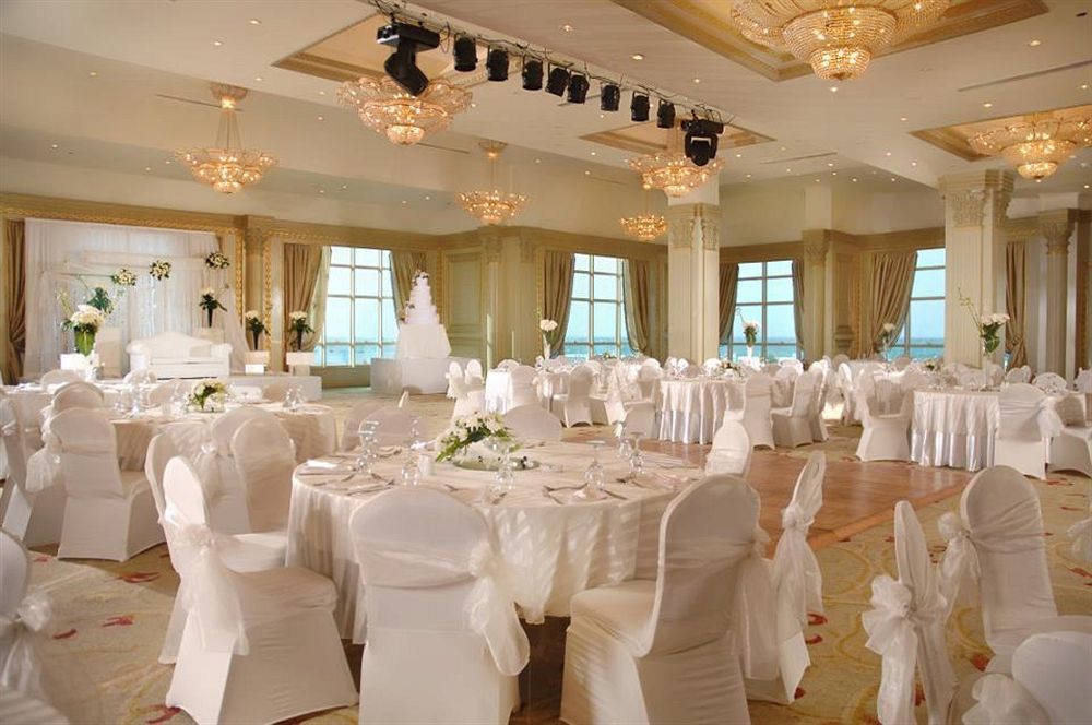 โรงแรมซันไรส์ อเล็กซ์ อเวนิว อเล็กซานเดรีย ภายนอก รูปภาพ The photo depicts an elegant banquet hall set up for a formal event, likely a wedding or reception. The room features several round tables covered with white tablecloths and adorned with floral centerpieces. Chairs are also dressed in white covers, c