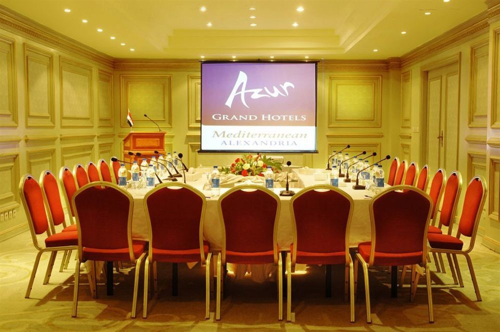 โรงแรมซันไรส์ อเล็กซ์ อเวนิว อเล็กซานเดรีย ภายนอก รูปภาพ The photo shows a conference room set up for a meeting or event. There is a large oval table surrounded by red chairs, and the table is equipped with microphones and bottles of water. In the background, there is a projector screen displaying the logo