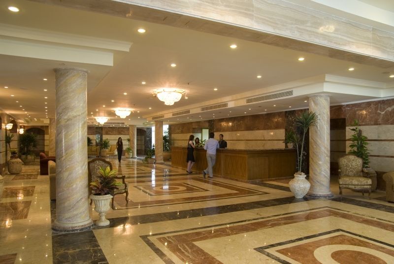 โรงแรมซันไรส์ อเล็กซ์ อเวนิว อเล็กซานเดรีย ภายนอก รูปภาพ The photo shows the interior of a spacious lobby, likely in a hotel. There are marble floors with intricate patterns, elegant lighting fixtures, and tall pillars. In the center, there is a reception desk where staff members are attending to guests. S